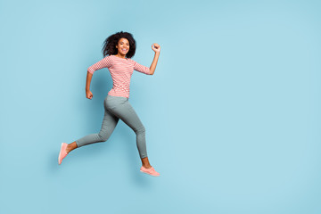 Fototapeta na wymiar Full length body size side profile photo of cheerful excited cute nice curly wavy youngster running jumping for sales wearing trousers pants striped t-shirt sneakers isolated over pastel blue color