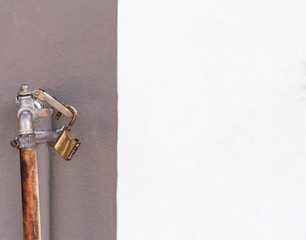 Old rusty faucet with old lock with space on white cement wall background, water supply 