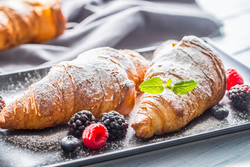 Freshly crispy croissants sprinkled sugar powder with raspberry blackberry and blueberry with...