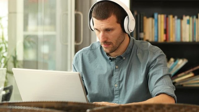 Serious man with headphones using a laptop sitting in a coffee shop or library