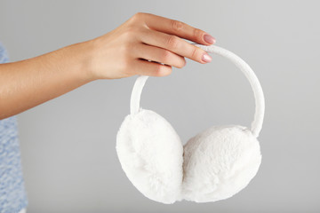 Female hand holding white furry earmuffs on grey background