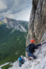 man and woman in their twenties climb a steep Via Ferrata for fun during their holidays