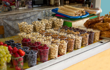 oriental bazaar selling berries grapes blueberries strawberries raspberries and cashews almonds pistachios hazelnuts walnuts peanuts in cups in portions stand in a row on the counter