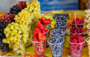 Fototapeta na wymiar oriental bazaar selling berries grapes blueberries strawberries raspberries in cups in portions stand in a row on the counter