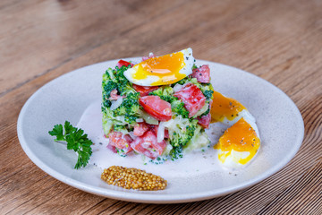 Delicious salad with broccoli, tomato, onion and boiled egg with cream sauce in plate on wooden background. Healthy food