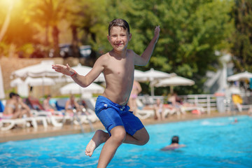 Naklejka premium Portrait of cheerful jumping European boy swimming in pool. He is enjoying his summer vacations.