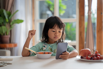 distracted kid using mobile phone while having breakfast on the table