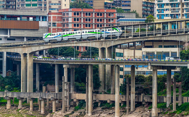 China. Monorail in the Chinese city of Chongqing, Yuzhong district. Metro train rides on a monorail. Transport, traffic flow, city blocks. Trees and bushes on the banks of the Jialing River.