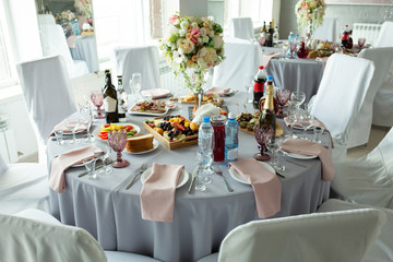 A wedding table for guests decorated with flowers and a tablecloth in a designer style with food and drinks. Decor and design of events, catering.