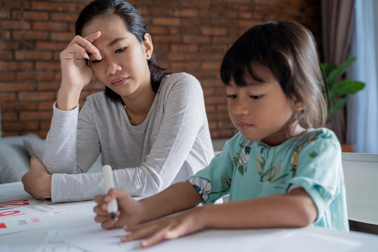 portrait of unhappy mother while teaching her daughter at home