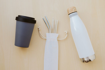 Reusable plastic free and eco friendly utensils. Metal drinking straws, bamboo coffee cup and water bottle, top view. Flat lay. Zero waste and conscious consumption concept. Reduce, reuse, recycle.