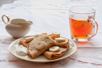 gluten free vegan homemade bananas pancake plate with sour cream and tea cup snack breakfast on white kitchen table background copy space