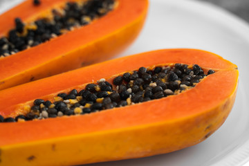 Half cut ripe papaya with seed on a white plate. Slices of sweet papaya with a white background. Halved papayas. Healthy exotic fruits. Vegetarian food.