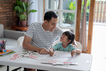 happy asian father teaching letter to her daughter at home. read and write lesson
