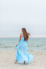 Fototapeta na wymiar Back of beautiful girl with long hair in a blue dress on the background of seaside