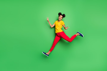 Fototapeta na wymiar Full body photo of nice dark skin lady jump high running competition participant came first to finish show v-signs wear yellow t-shirt red pants isolated green background