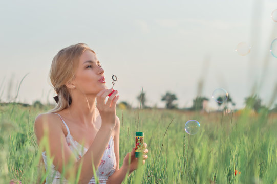 Blonde girl with log hair blowing soap bubbles in summer park