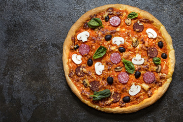 pizza with mushrooms, olives, spinach and sausage and greens on a dark background