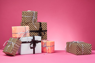 Different sizes, colorful, striped and plain paper gift boxes tied with ribbons and bows on a pink...
