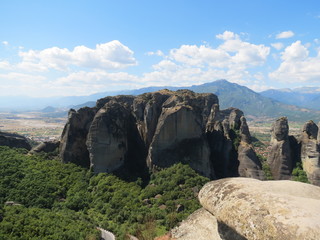 Huge cliffs in the mountains of Thessaly in Northern Greece against the background of clouds and blue sky surrounded at the foot by trees