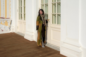 young beautiful pretty lady woman posing in a long green and brown dress gown overcoat on terrace and steps of historical palace in Oranienbaum near Saint Petersburg, Russia