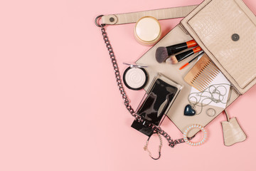 Fashion concept : Flat lay of brown leather woman bag open out with cosmetics, accessories and smartphone on pink background