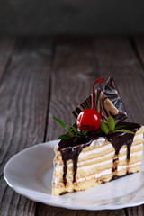 A biscuit cake is filled with chocolate with slices of chocolate tile, cherry and green leaf on wooden background.