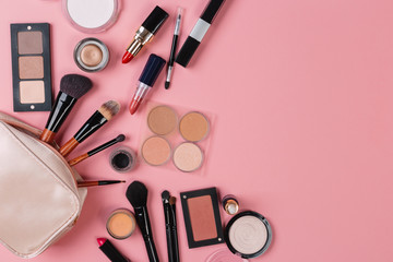 A pink makeup bag with cosmetic beauty products spilling out on to a pastel colored background, with empty space at side