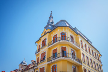 Facade of a typical European yellow building, with a gable roof and blue sky