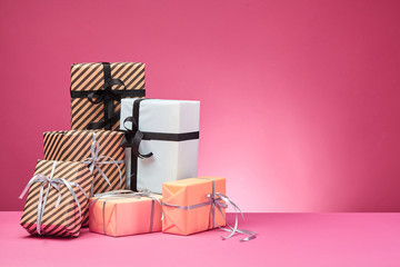 Different sizes, colorful, striped and plain paper gift boxes tied with ribbons and bows on a pink surface and background. Close-up, copy space.