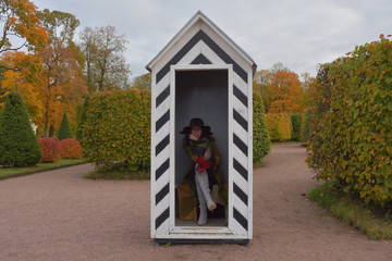 young pretty beautiful girl woman in black hat and green and yellow long overcoat posing in a garden guard's booth in autumn colorful garden park