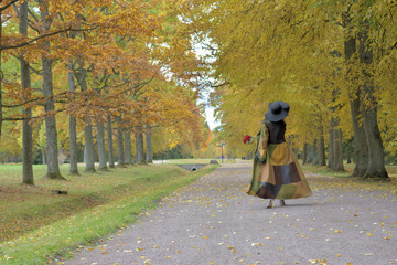 young beautiful pretty lady woman posing in a long green and brown dress gown overcoat walks down a lonely alley in the garden of the palace in Oranienbaum near Saint Petersburg, Russia