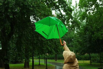 Woman with broken green umbrella in park on rainy day