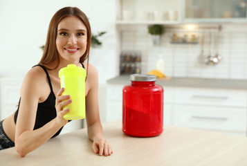 Young woman drinking protein shake at table indoors