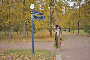 young beautiful pretty lady woman posing in a long green and brown dress gown overcoat walks down a lonely alley in the garden and looks at the information sign with emotions