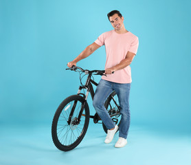 Fototapeta na wymiar Handsome young man with modern bicycle on light blue background