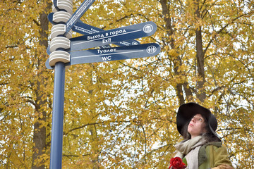 young beautiful pretty lady woman posing in a long green and brown dress gown overcoat walks down a lonely alley in the garden and looks at the information sign with emotions