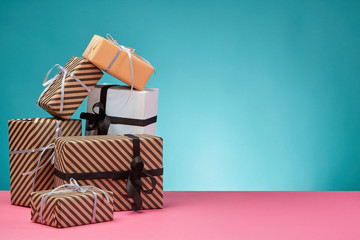 Different sizes, colorful, striped and plain paper gift boxes tied with ribbons and bows on a pink surface and blue background. Close-up, copy space.
