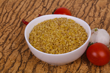 Raw bulgur in the bowl with tomatoes and garlic