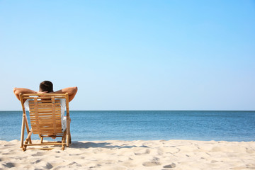 Fototapeta Young man relaxing in deck chair on sandy beach obraz