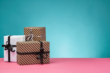 Different sizes, colorful, striped and plain paper gift boxes tied with ribbons and bows on a pink surface and blue background. Close-up, copy space.
