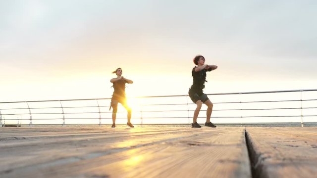 Two young women in ems suit doing exercise on seashore at sunrise