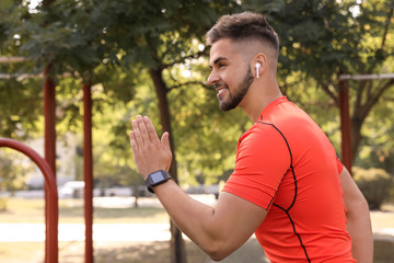 Obraz premium Young man with wireless headphones listening to music while exercising on sports ground. Space for text