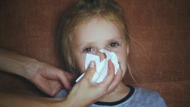 A mother helps her sick little daughter blow her nose