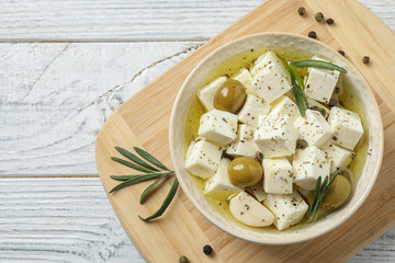 Flat lay composition with pickled feta cheese in bowl on white wooden table