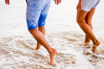 Couple of lovers walking together on the sea beach at sunset - Feet close up, Romantic date atmosphere.