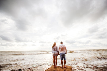 Couple of lovers walking together on the sea beach at sunset - Stading with back and looking at...