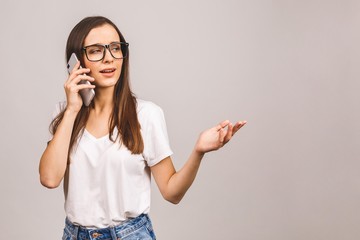Portrait of a furious young woman talking on mobile phone isolated over grey background.