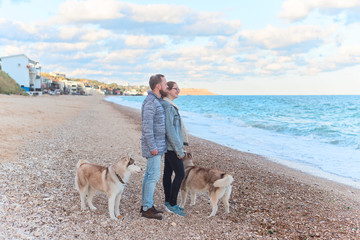 Couple walking along the coast with two husky dogs