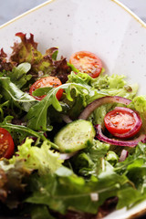 bowl of salad with vegetables and greens, with tomato, cucumber and onions on rustic table